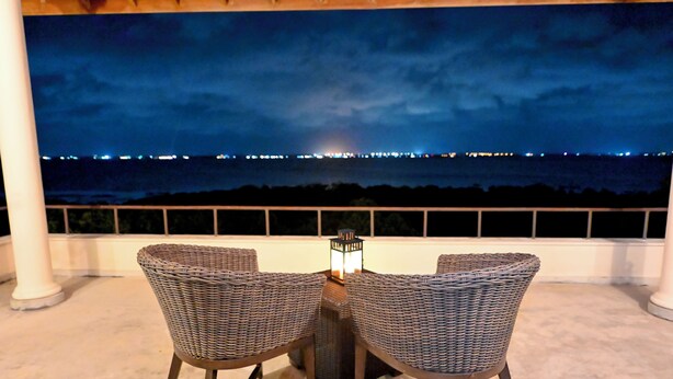 Un área de estar al aire libre con dos sillas de mimbre y una mesa, con vistas a un paisaje urbano nocturno.