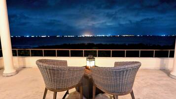 An outdoor seating area with two wicker chairs and a table, overlooking a cityscape at night.