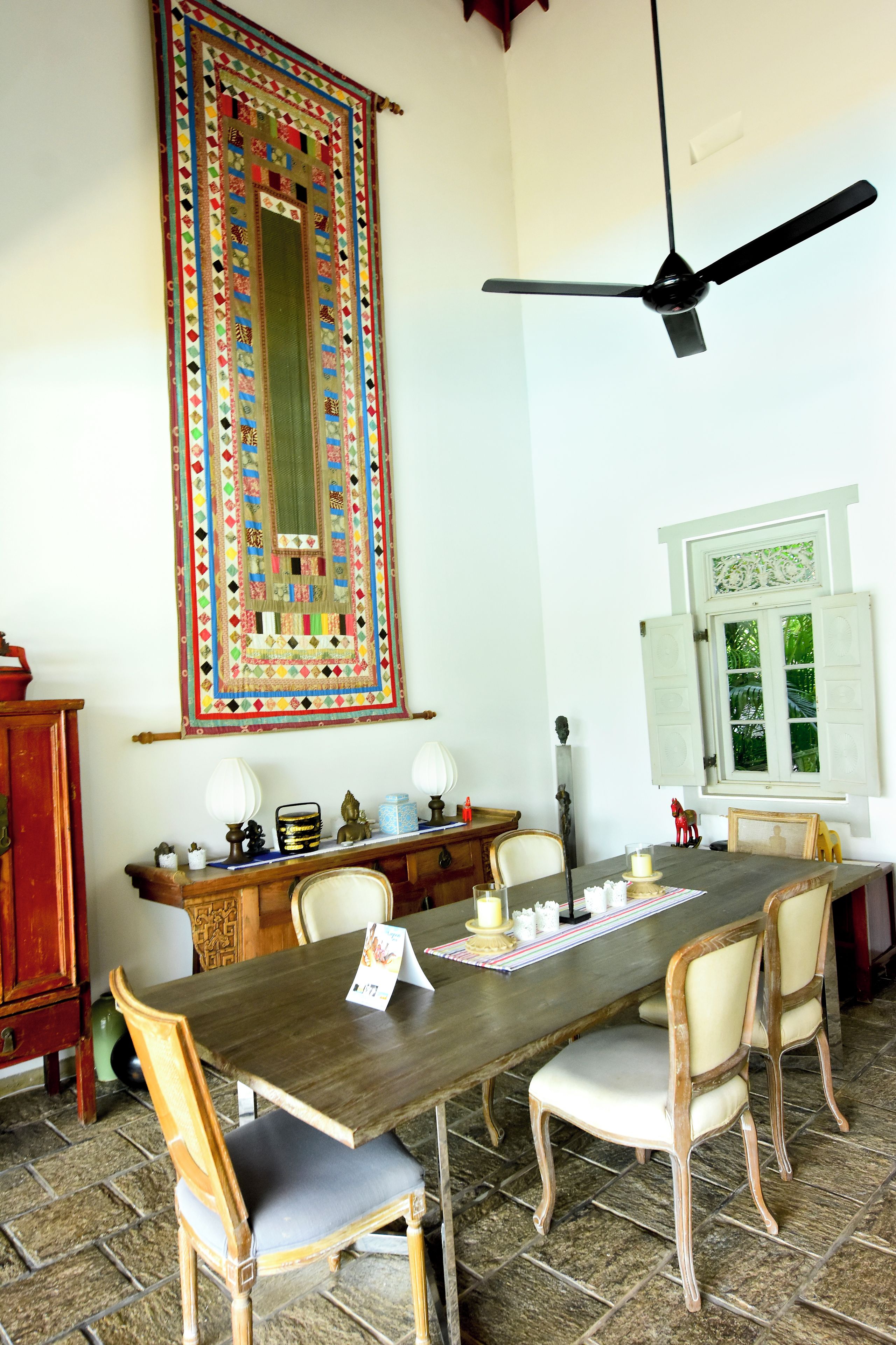 A dining area with a wooden table, chairs, a ceiling fan, and a decorative hanging piece.
