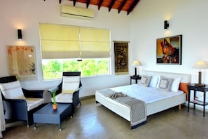 A bedroom with a bed, two chairs, a small table, a nightstand, a lamp, and a window with a view of greenery. - Hotel with 4 bedrooms and AC in peaceful Negombo (Negombo)