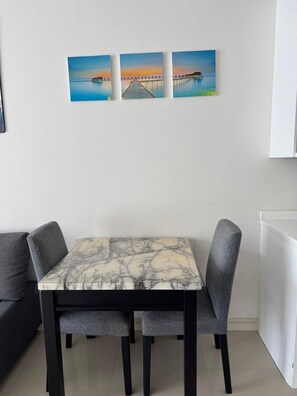 Ein Essbereich mit einem Marmortisch und grau gepolsterten Stühlen, einer weißen Wand mit drei gerahmten Bildern und einem weißen Schrank.