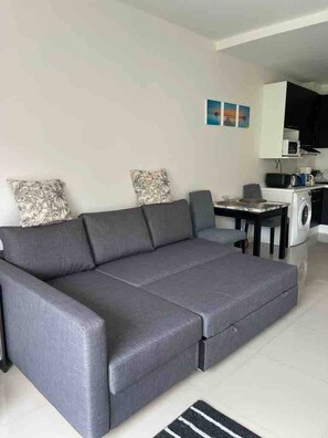 Ein moderner Wohnbereich mit einem grauen Sofa, einem Esstisch und einer Küche im Hintergrund.