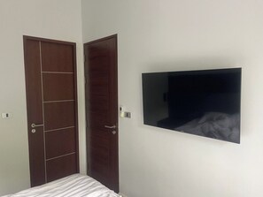 Una stanza con un letto, una TV fissata al muro e due porte.