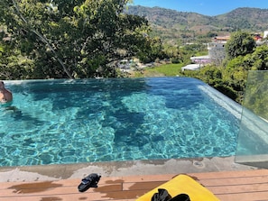 A clear swimming pool with a wooden deck and a yellow cushion, surrounded by lush greenery and a view of a hillside. - Utopia D Private & Quiet · 1BR · Pets OK · 500Mbps (Tambon Rawai)