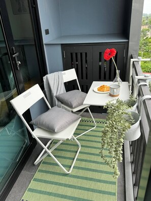 A balcony with two white chairs, a small table with a plate of food, a vase with a red flower, and a hanging plant. - Top-Floor Sea-View Studio, Nai Harn, Rooftop Pool (Tambon Rawai)