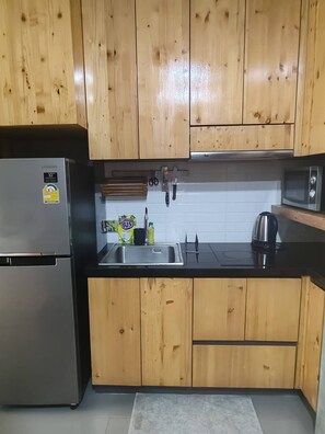 Ett kök med träskåp, ett kylskåp i rostfritt stål, en mikrovågsugn och en diskho.
