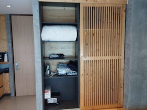 A room with a built-in wardrobe featuring a wooden slat design, a bed with a white mattress, and a small ironing station with a box labeled 'STEAM IRON'. - Nai Harn Studio, Steps to Everything, Pool, Gym (Tambon Rawai)