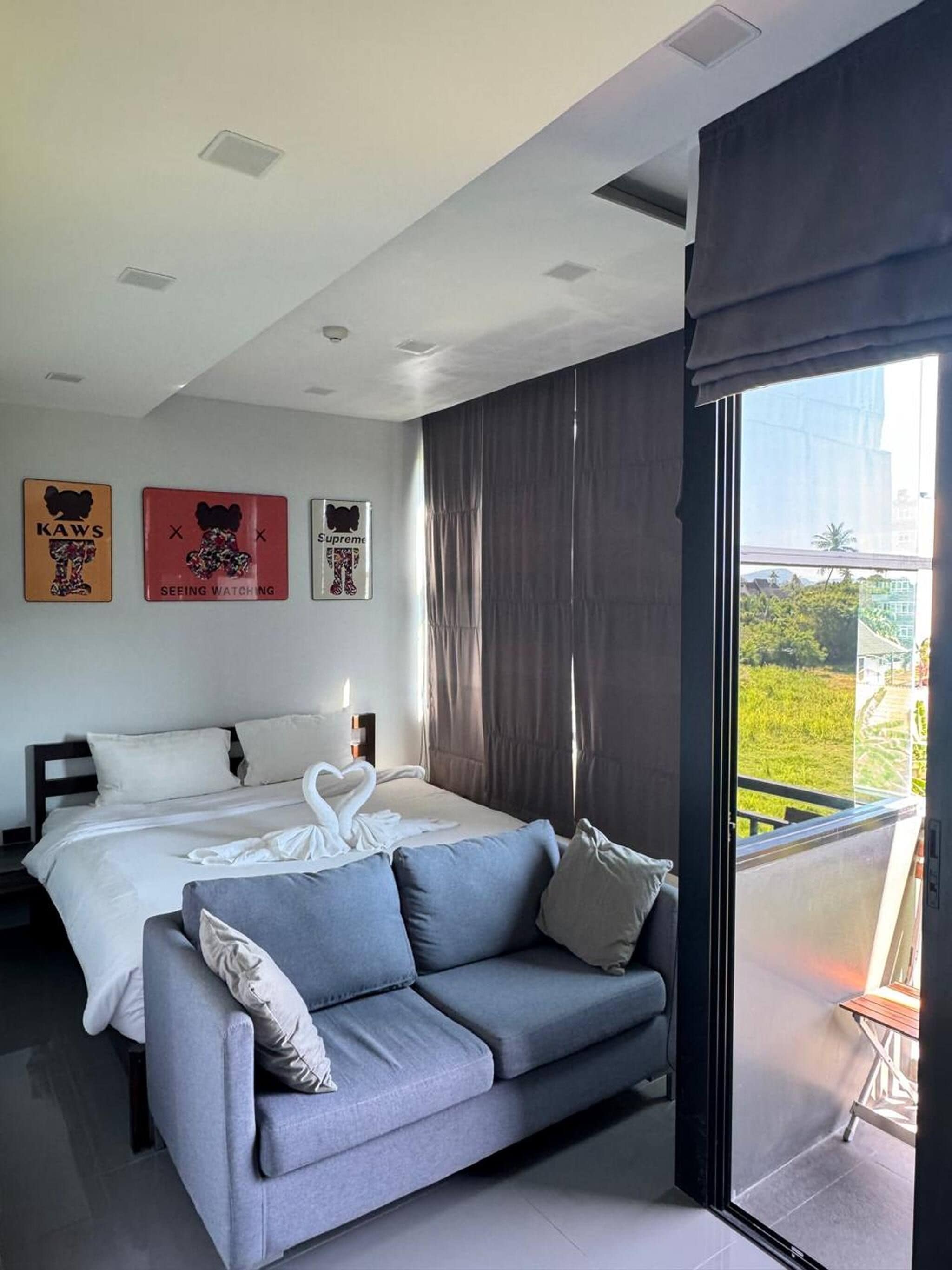 A modern bedroom with a large bed, a sofa, and a balcony with a view.