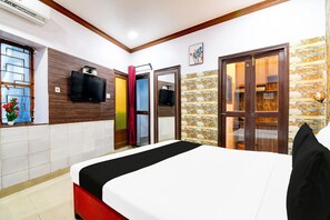 Ein Hotelzimmer mit Bett, Fernseher, Fenster mit Vorhängen, Tür und Wand mit Musterdesign.
