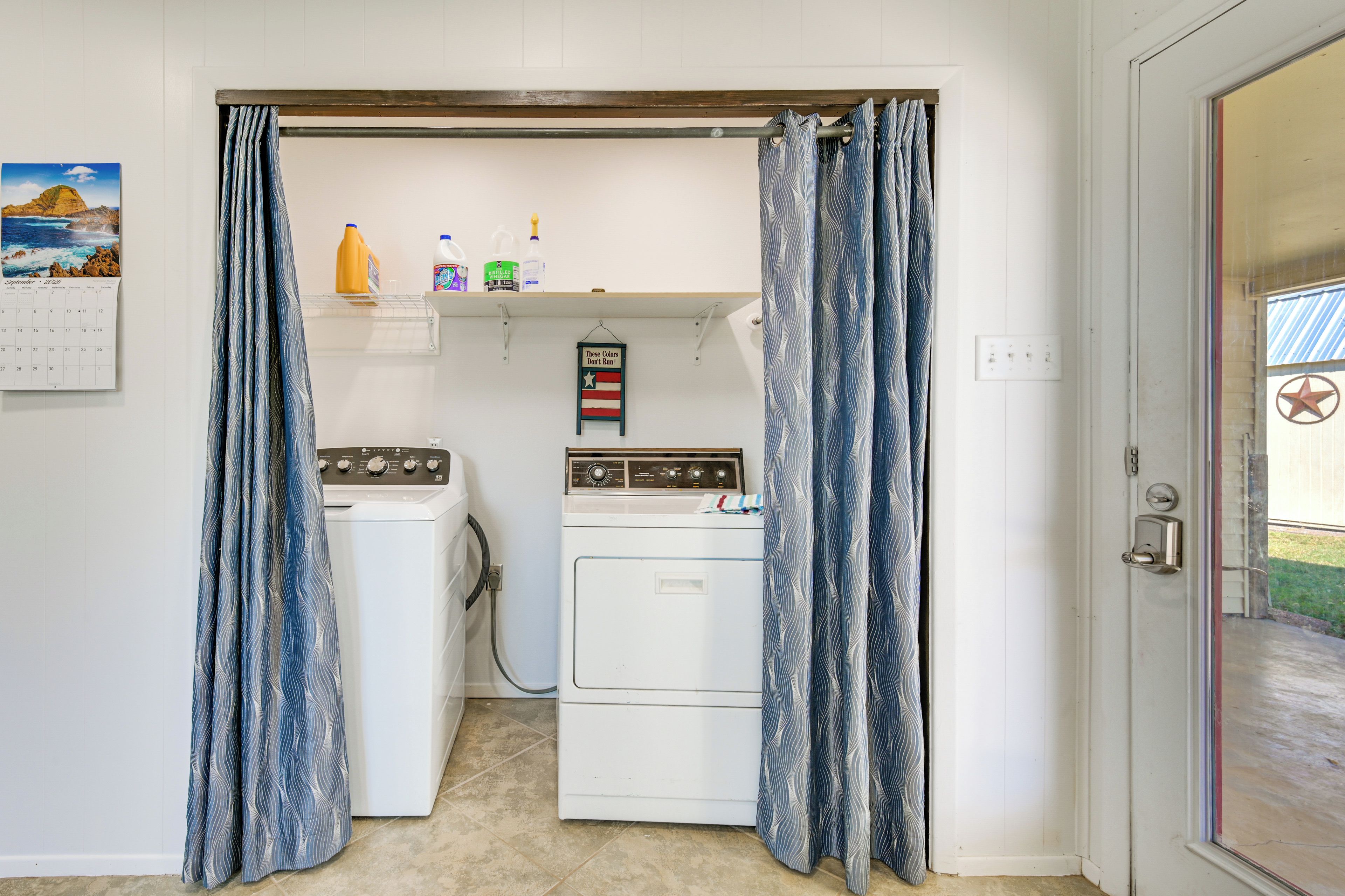 A laundry room with two washing machines, a calendar, and cleaning supplies on a shelf.