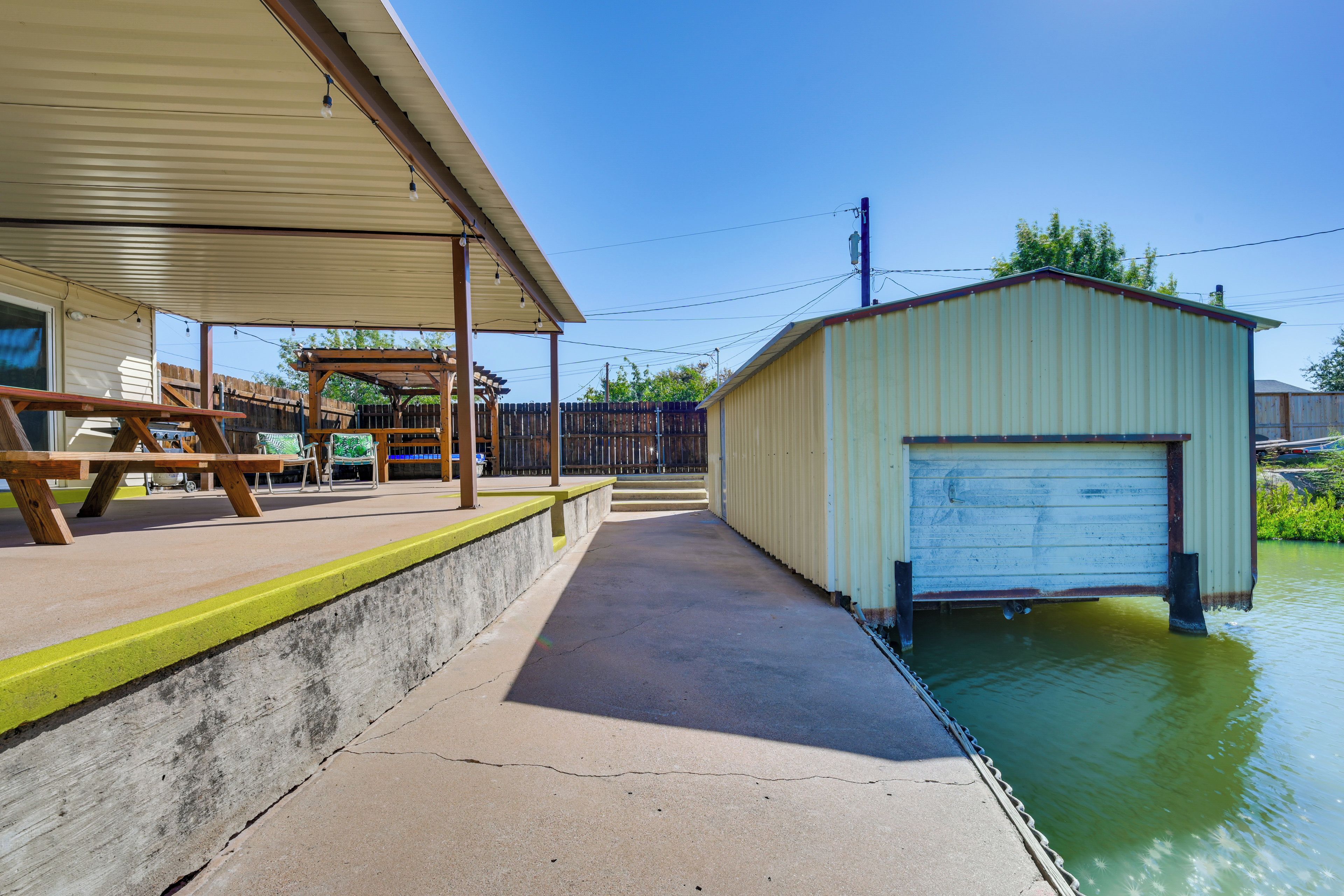 A covered outdoor area with a concrete walkway, a wooden bench, and a small building with a garage door.