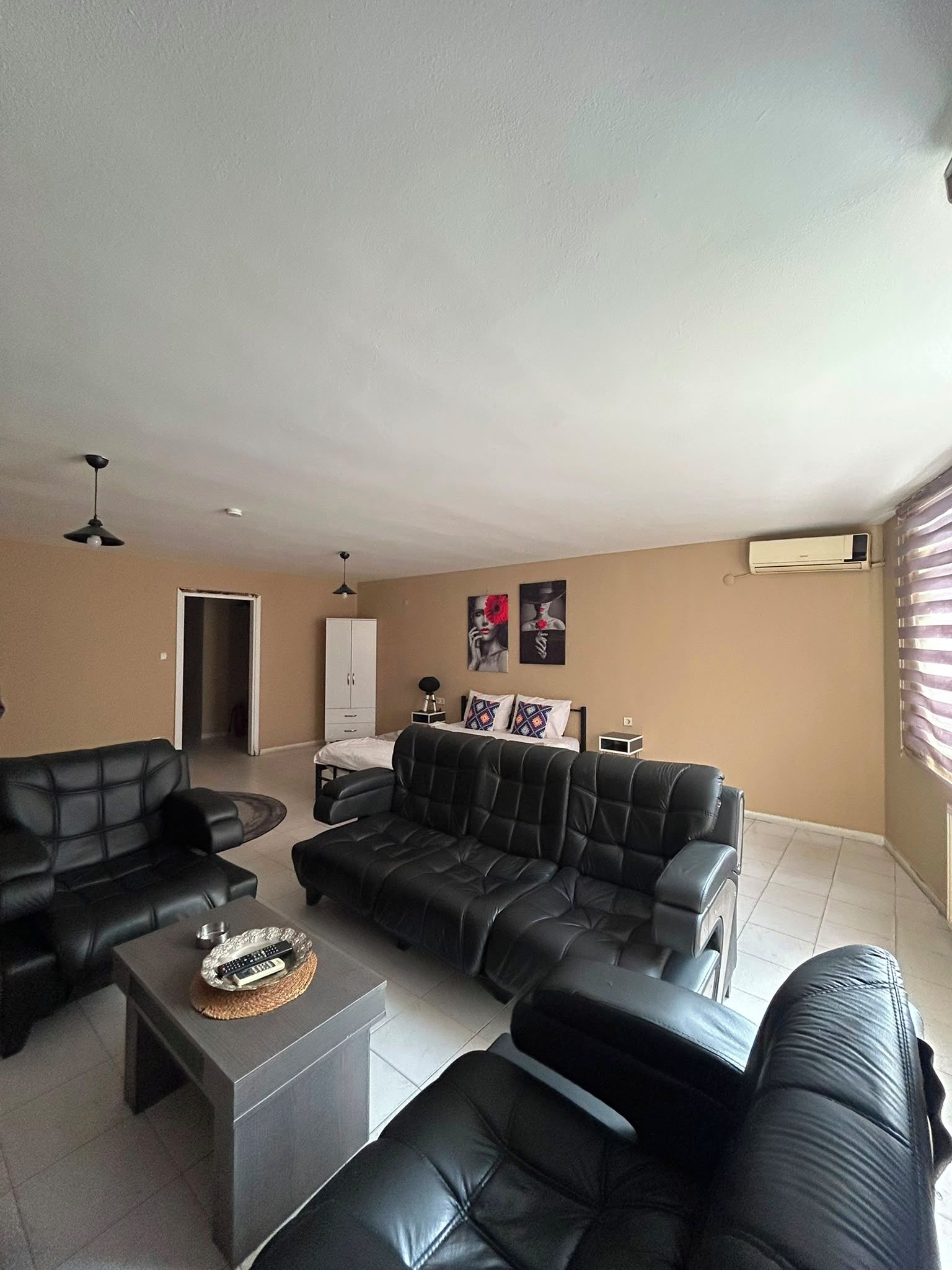 A living room with a sofa set, a coffee table, and a TV. There is a door leading to another room and a window with blinds.