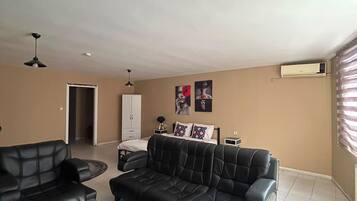 A living room with a sofa set, a coffee table, and a TV. There is a door leading to another room and a window with blinds.