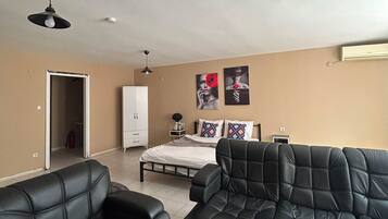 A living room with two black leather sofas, a bed with a white headboard, a white wardrobe, and a ceiling fan.