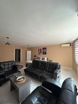 A living room with a sofa set, a coffee table, and a TV. There is a door leading to another room and a window with blinds. - No 19 suite pendik otel 3 (Pendik)