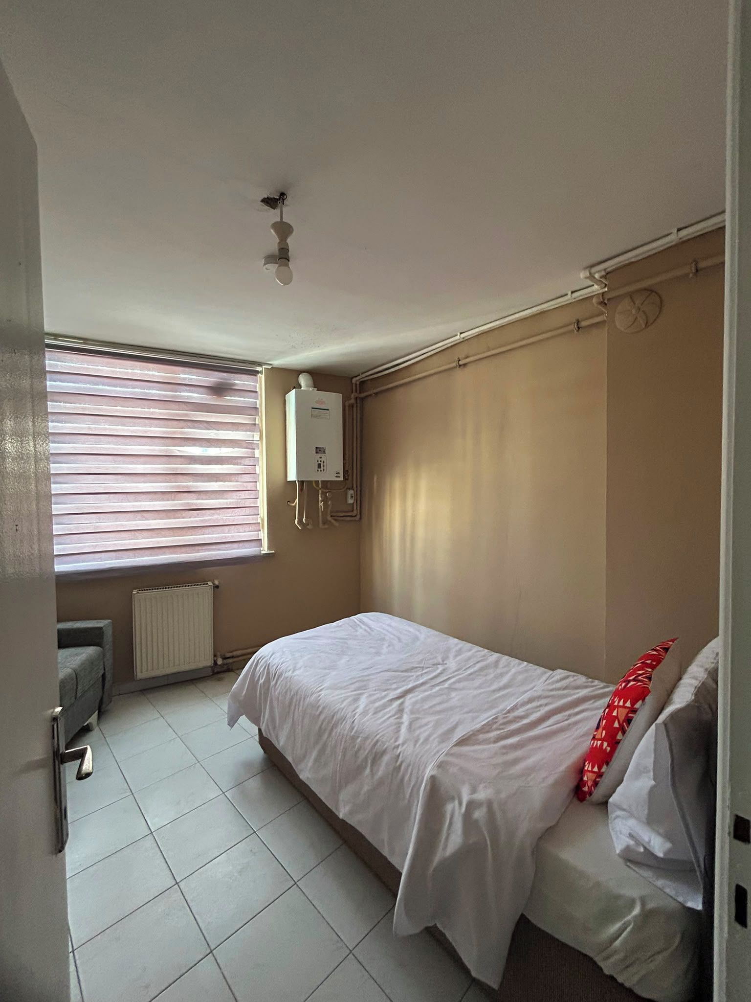 A bedroom with a bed, a radiator, a window with blinds, and a ceiling fan.