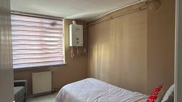 A bedroom with a bed, a radiator, a window with blinds, and a ceiling fan.