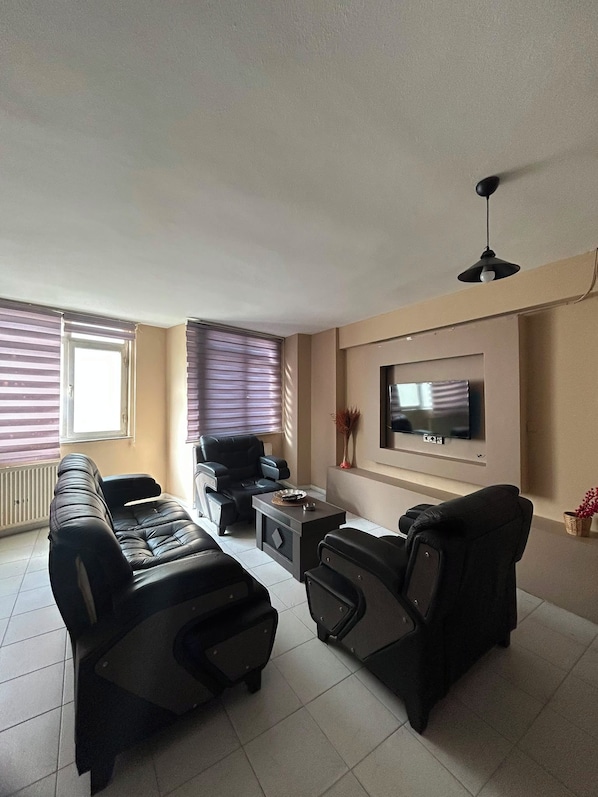 Ein Wohnzimmer mit einer Sofagarnitur, einem Couchtisch, einem an der Wand befestigten Fernseher und einem Deckenventilator.