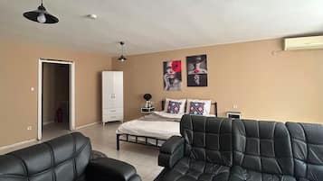 Ein Wohnzimmer mit zwei schwarzen Ledersofas, einem Bett mit weißem Kopfteil, einem weißen Kleiderschrank und einem Deckenventilator.