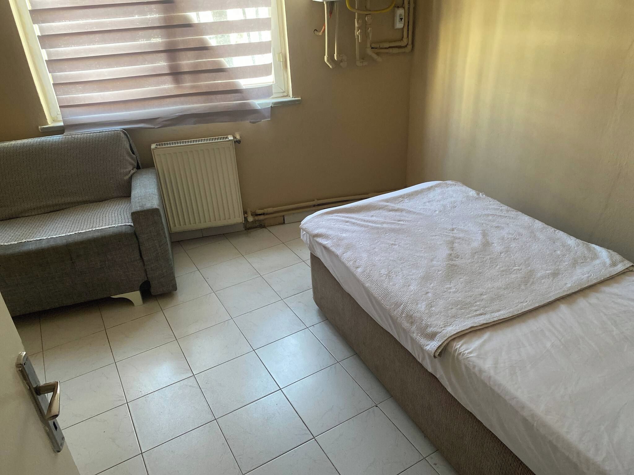 A small, sparsely furnished room with a radiator, a sofa, and a single bed.