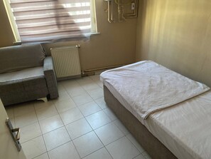 Una habitación pequeña y poco amoblada con un radiador, un sofá y una cama individual.