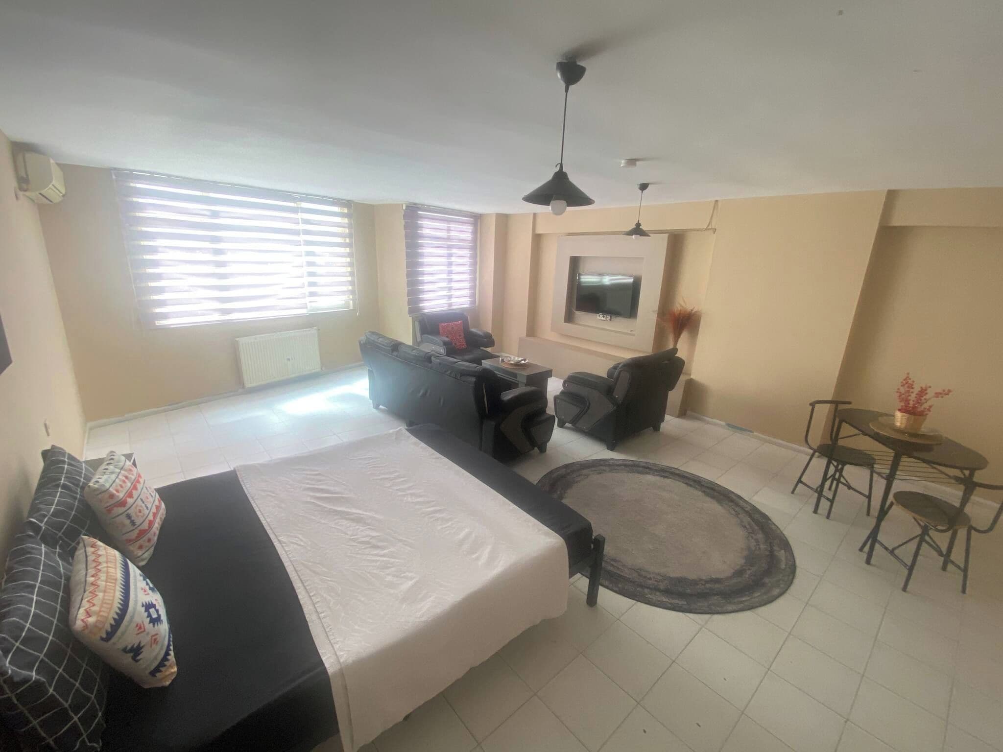 A modern living room with a sofa, a dining table with chairs, a TV mounted on the wall, and a ceiling fan.