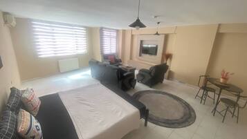 A modern living room with a sofa, a dining table with chairs, a TV mounted on the wall, and a ceiling fan.