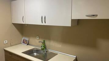 Una kitchenette con un lavamanos de acero inoxidable, una botella verde de lavavajillas y un refrigerador pequeño.