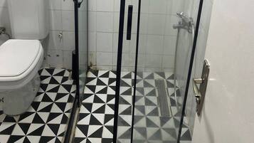 A bathroom with a toilet, a shower with a glass door, and a tiled floor with a geometric pattern.