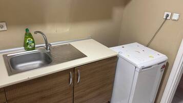 A compact kitchen with a sink, a bottle of dish soap, and a small refrigerator.