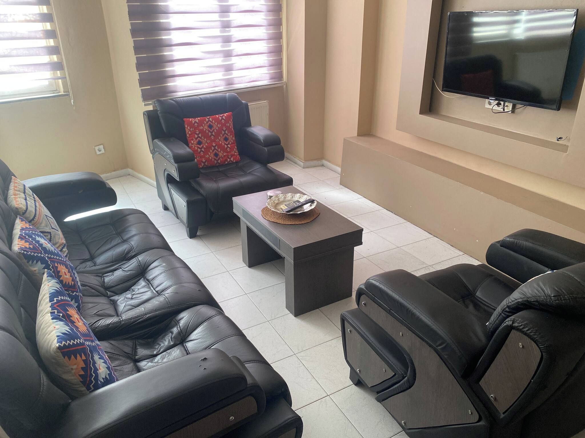 A living room with black leather sofas, a coffee table, and a flat-screen TV mounted on the wall.