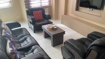 A living room with black leather sofas, a coffee table, and a flat-screen TV mounted on the wall.