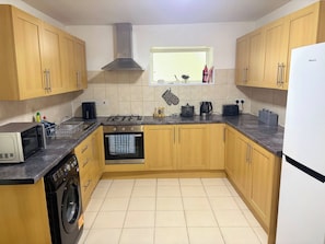 A kitchen with wooden cabinets, a stove, a dishwasher, and a window with a view. - Luxurious 3-Bedroom Apartment in Swansea City Centre (Swansea)