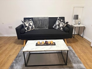 A modern living room with a black sofa, two patterned throw pillows, a marble coffee table with candles, and a small side table with a lamp. - Luxurious 3-Bedroom Apartment in Swansea City Centre (Swansea)