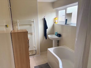 A bathroom with a white bathtub, a sink, a towel rack, and a wooden cabinet. - Luxurious 3-Bedroom Apartment in Swansea City Centre (Swansea)