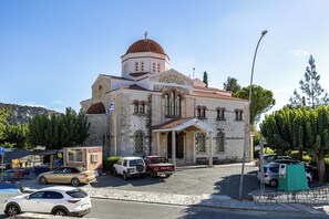 A church with a dome and a bell tower, surrounded by parked cars and trees. - Troodos View Garden House - Trimiklini (Trimiklini)