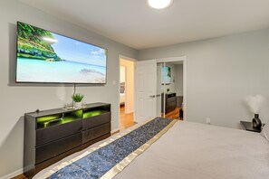 A bedroom with a bed, a TV mounted on the wall, a console table, and a door leading to another room.