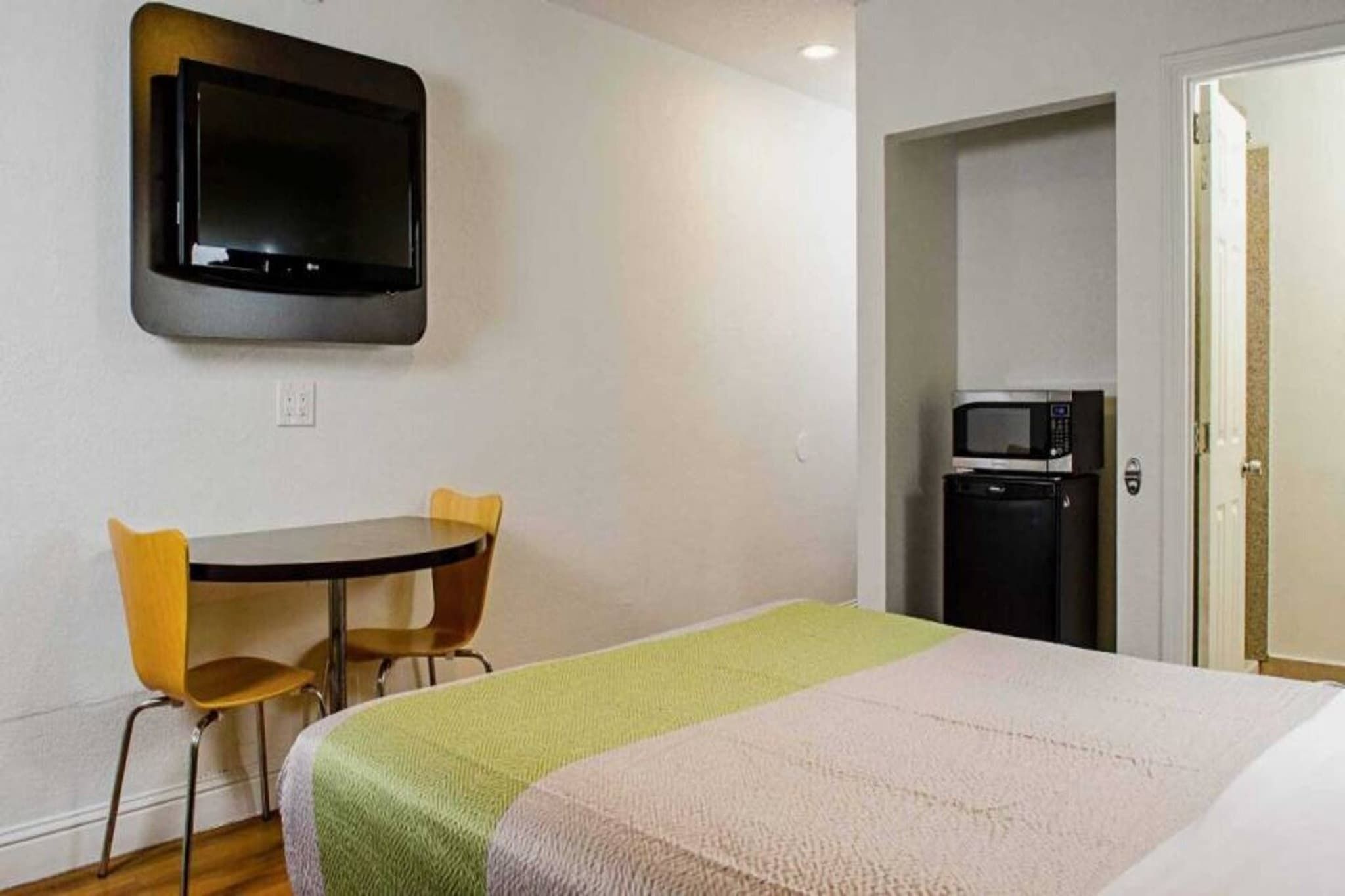 A hotel room with a bed, a table with two chairs, a television mounted on the wall, and a microwave in the corner.