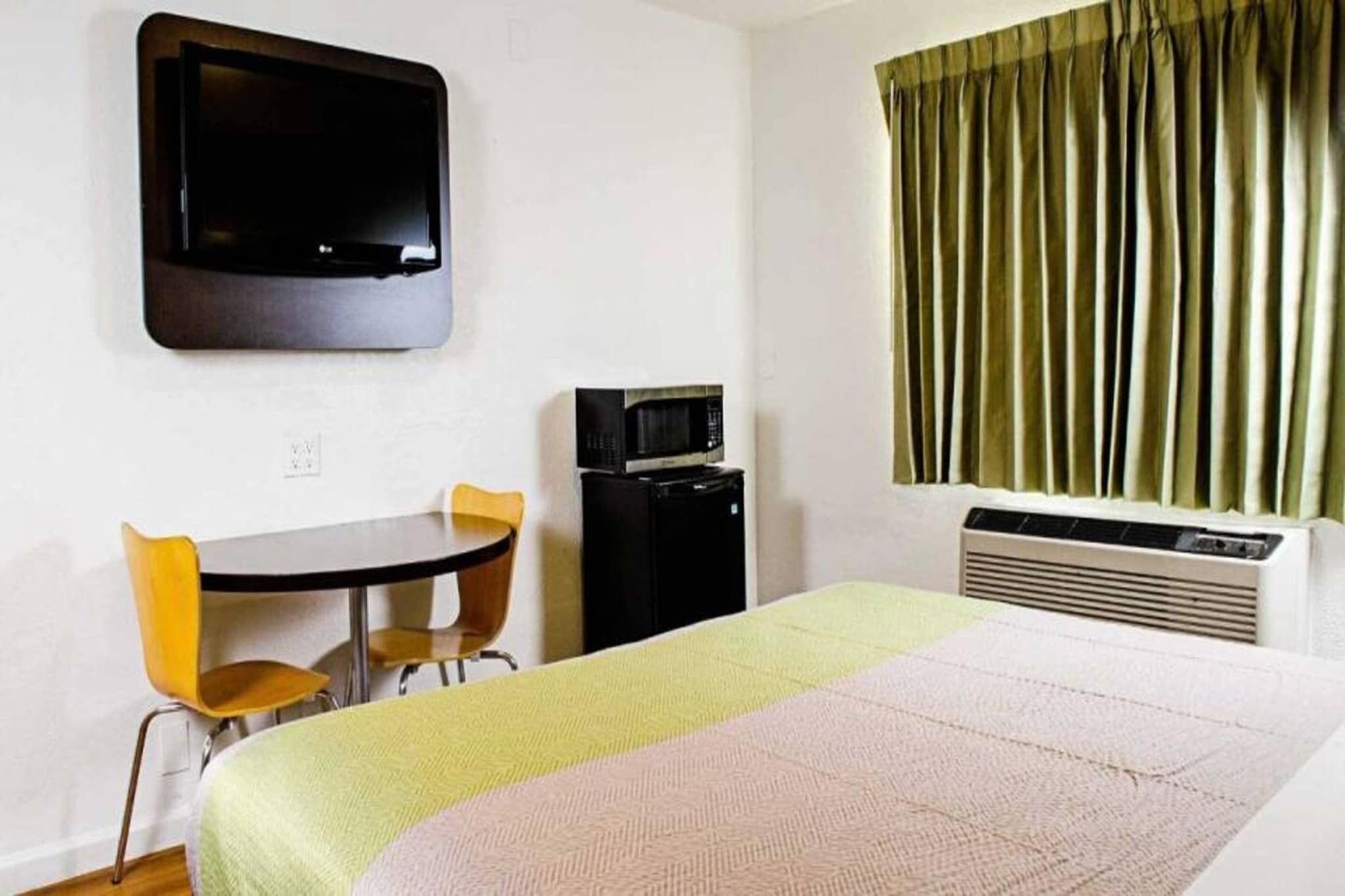 A hotel room with a bed, a desk with two chairs, a television, a microwave, and a window with curtains.