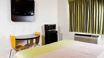 A hotel room with a bed, a desk with two chairs, a television, a microwave, and a window with curtains.