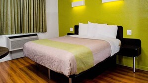Habitación de hotel con una cama, una mesita de noche, una lámpara, una ventana con cortinas y un aire acondicionado de pared.