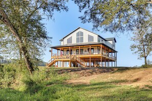 A two-story wooden house with a balcony, surrounded by trees and grassy area. - 'River Bank' Spacious Waterfront Group Getaway (Nashville)