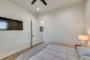 Ein Schlafzimmer mit einem Bett, einem an der Wand montierten Fernseher, einer Tür und einem Nachttisch mit Lampe.