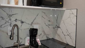 A kitchen with a stainless steel sink, a black coffee maker, a microwave, and a marble backsplash.