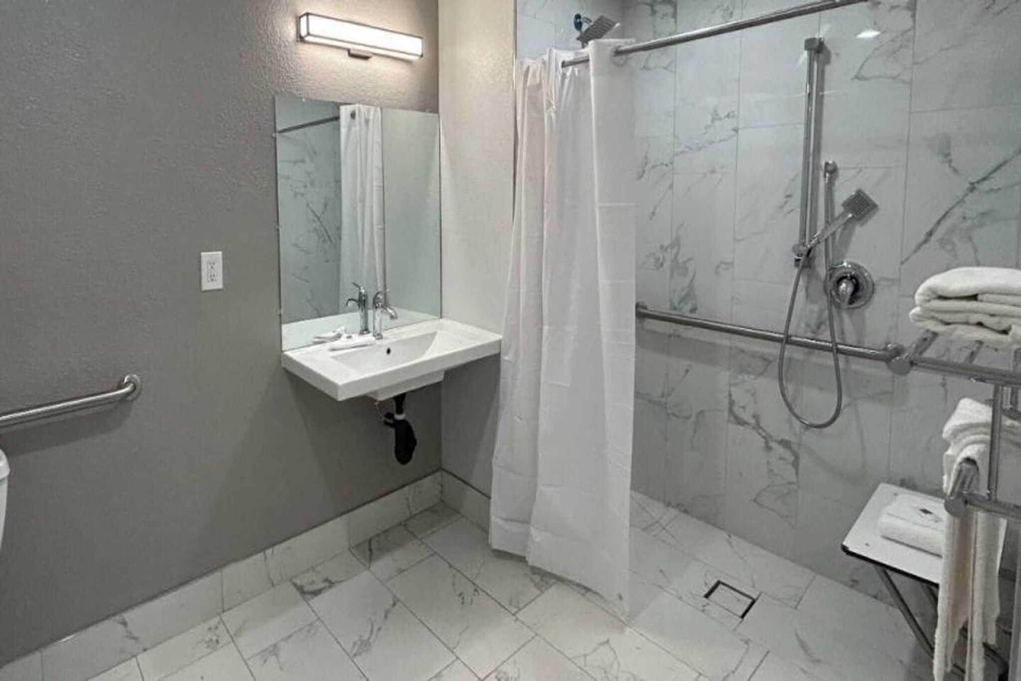 A bathroom with a white sink, a mirror, a shower with a glass door, and a towel rack.