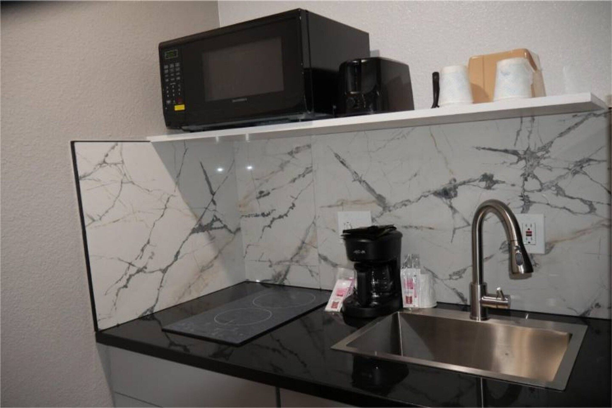 A kitchen with a black microwave, a coffee maker, and a stainless steel sink.