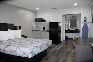 Habitació d'hotel amb llit, escriptori, petita cuina i bany.