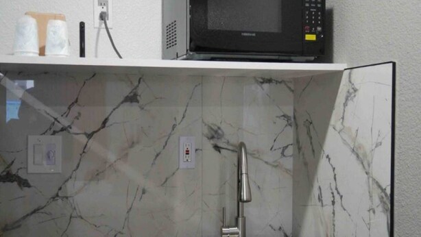 Une cuisine avec un dosseret en marbre, un évier en acier inoxydable et un micro-ondes posé sur une étagère.