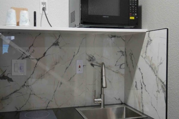 Una cuina amb un respatller de marbre, un obrador d'acer inoxidable i un microones a una estantalia.
