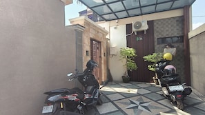 Une cour où sont garées deux motos, avec un sol carrelé, une porte en bois et une petite plante en pot.